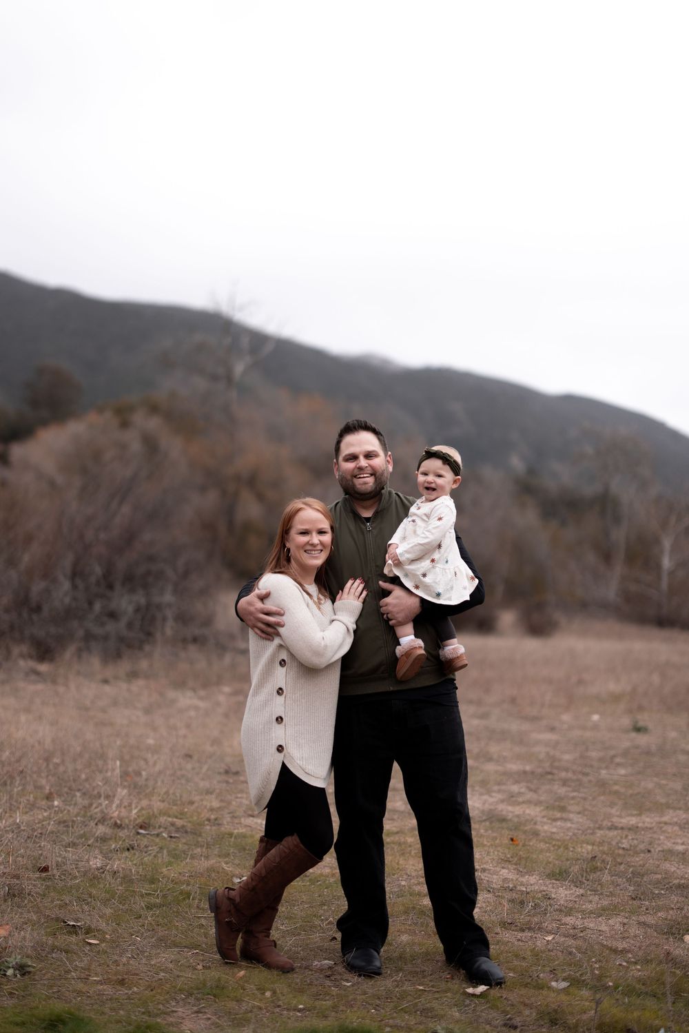 Family stands together in casual attire against mountain backdrop during outdoor photo session.