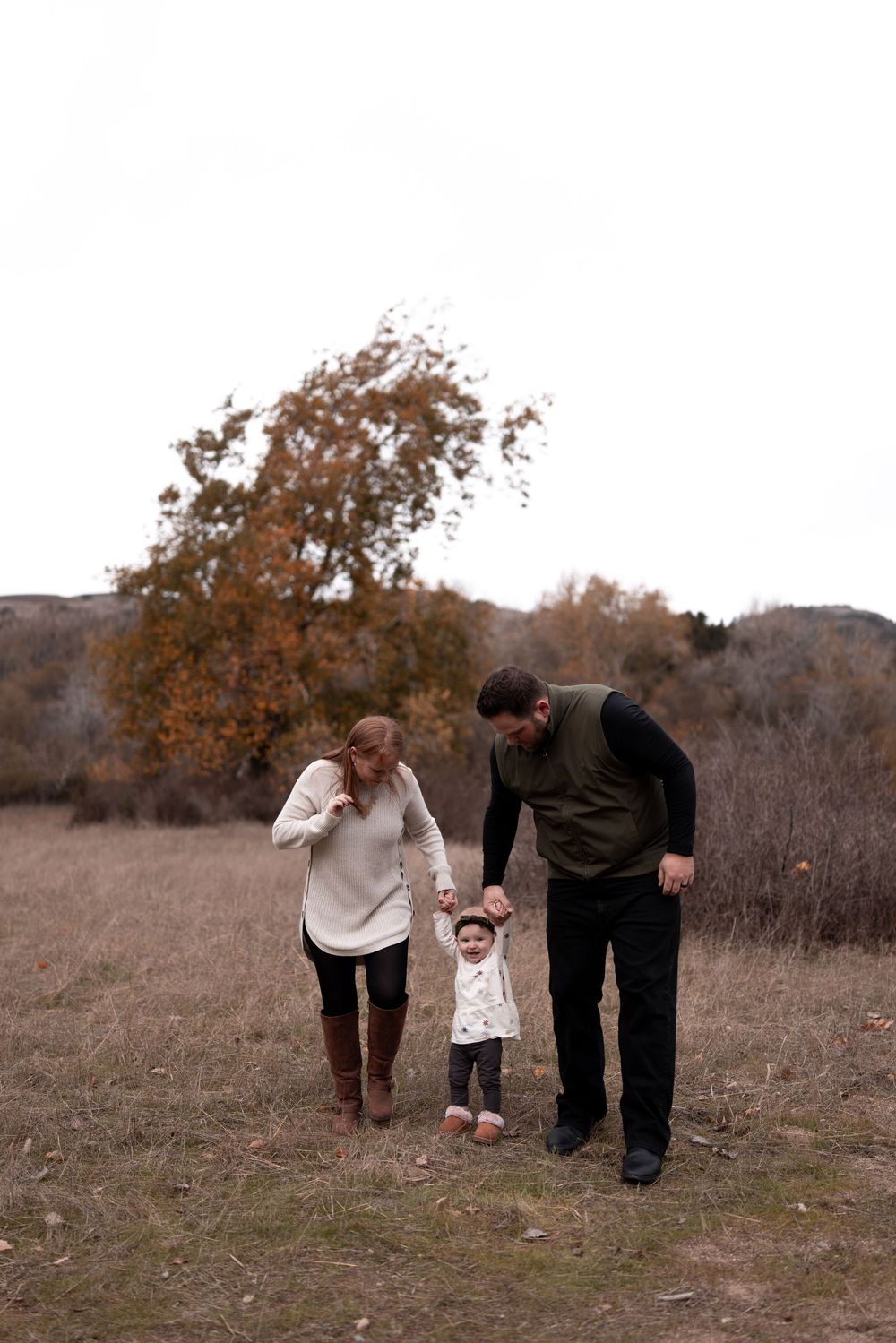 A family walking together through an autumn field holding hands with their toddler.