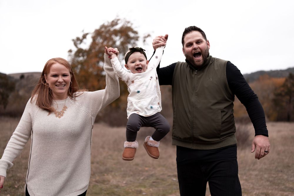 A family playing together outdoors as they lift their laughing toddler in the air.