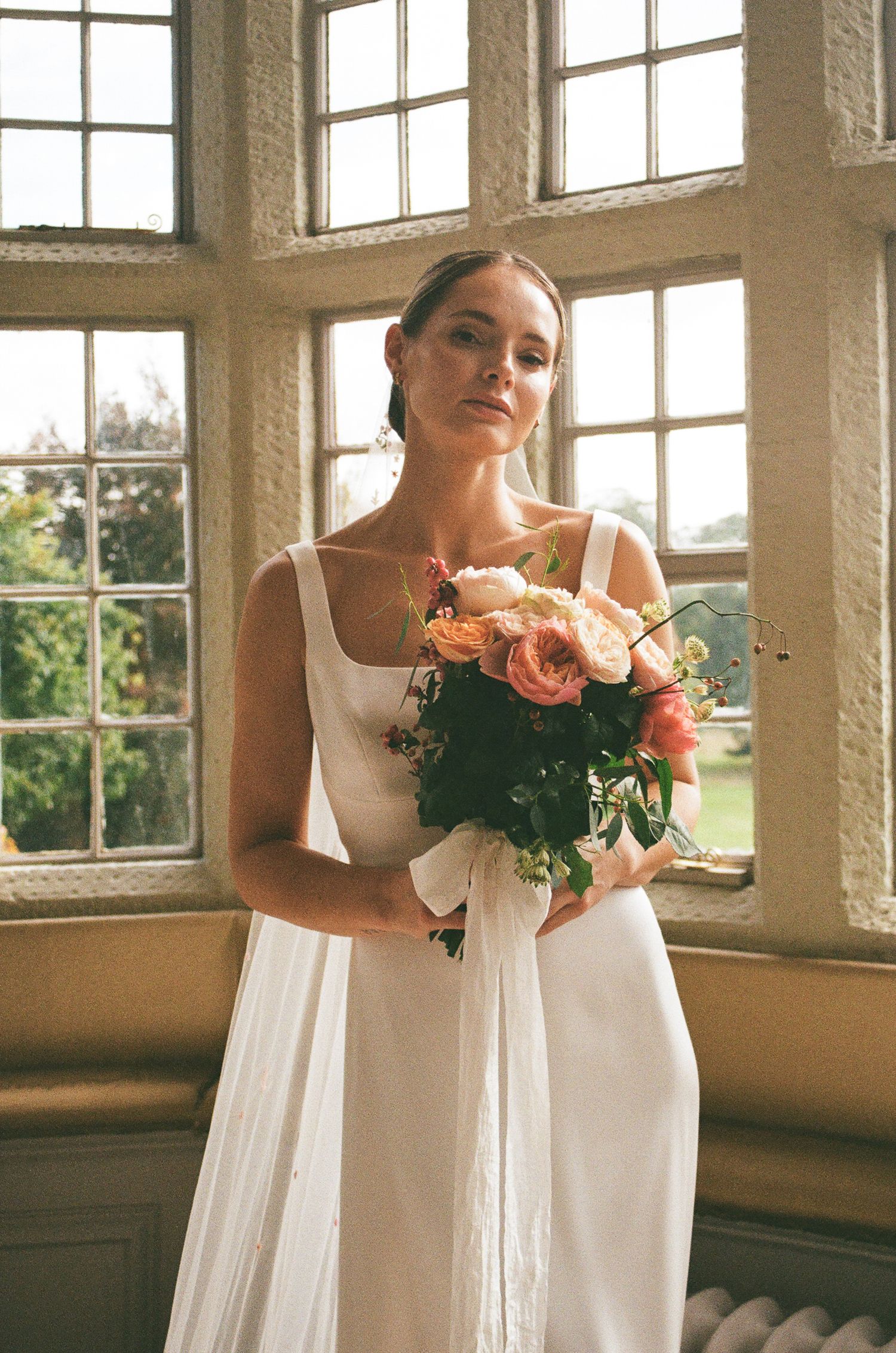 35mm film photo of a bride in an elegant wedding gown standing in the bridal suite of Howsham Hall.