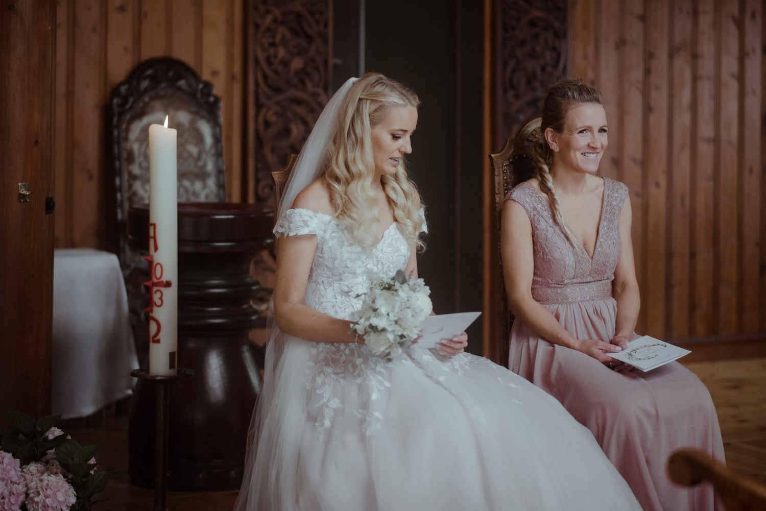 A wedding scene showing a bride in white dress and bridesmaid in pink dress during the ceremony.
