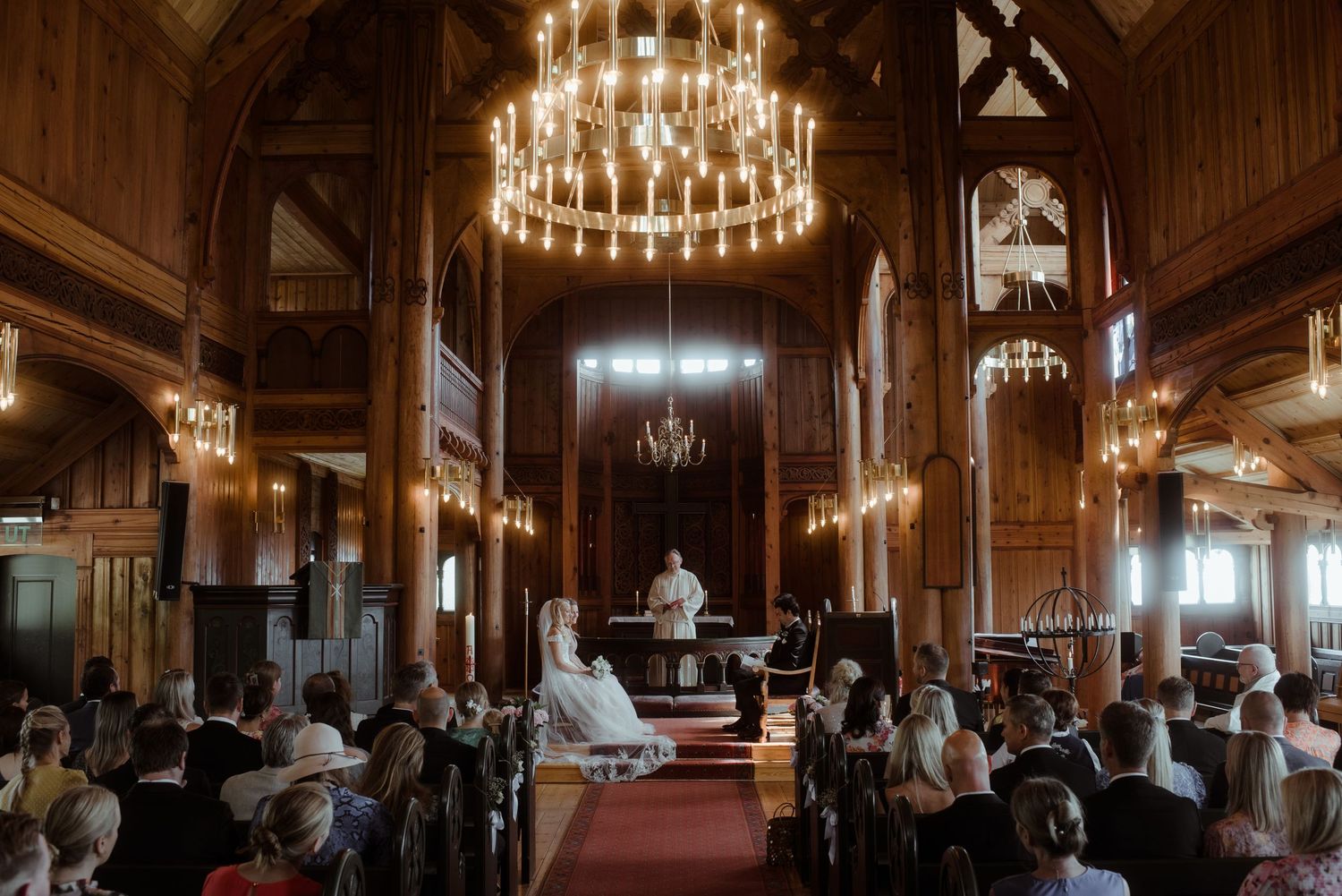 A majestic church ceremony with dramatic lighting from chandeliers illuminating the wooden interior.