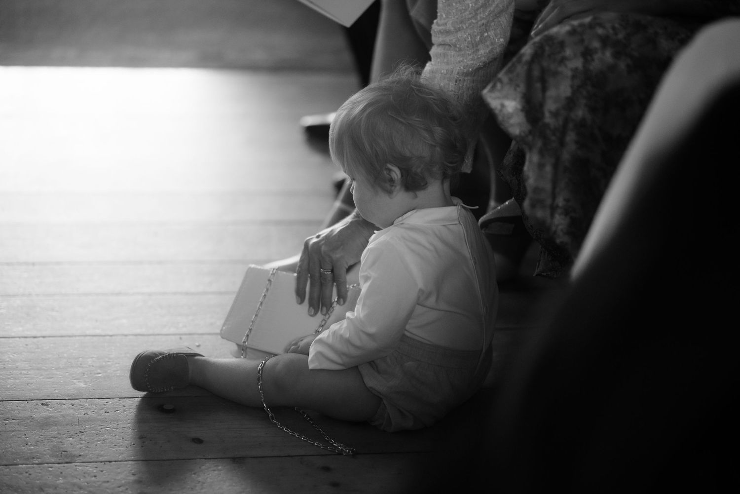 Young child sitting on floor during wedding ceremony captured in black and white.
