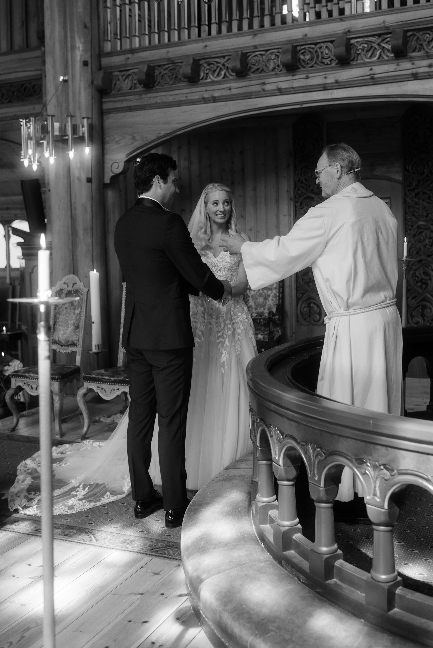 A wedding ceremony takes place in an ornate church with carved wooden details and candlelight.
