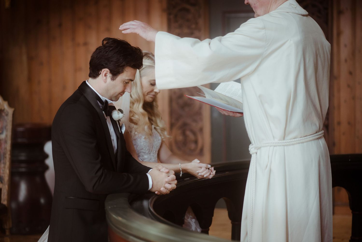 Wedding ceremony moment during a blessing in a wood-paneled church interior.