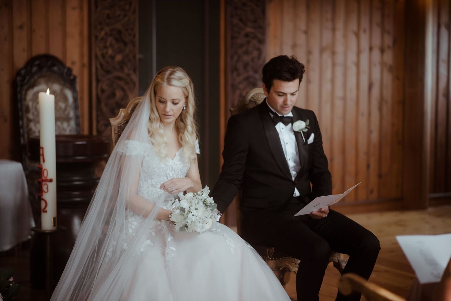 Wedding ceremony in progress inside a grand wooden chapel with candles lit.