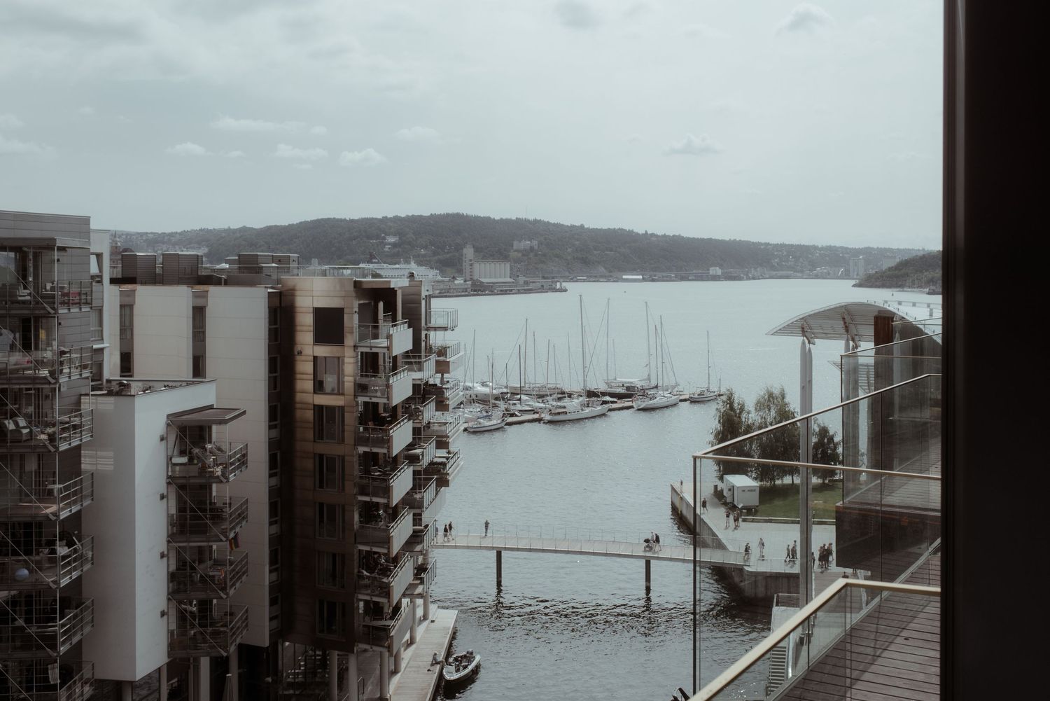 Moody cityscape view of a marina with boats and modern apartment buildings on an overcast day.