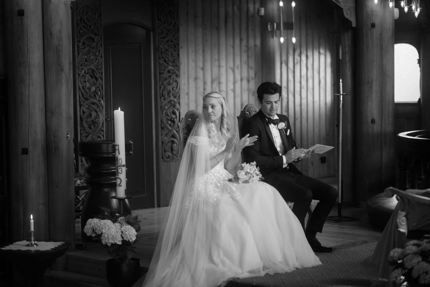 A wedding couple poses by candlelight in a gothic church interior with ornate wooden details and romantic lighting.
