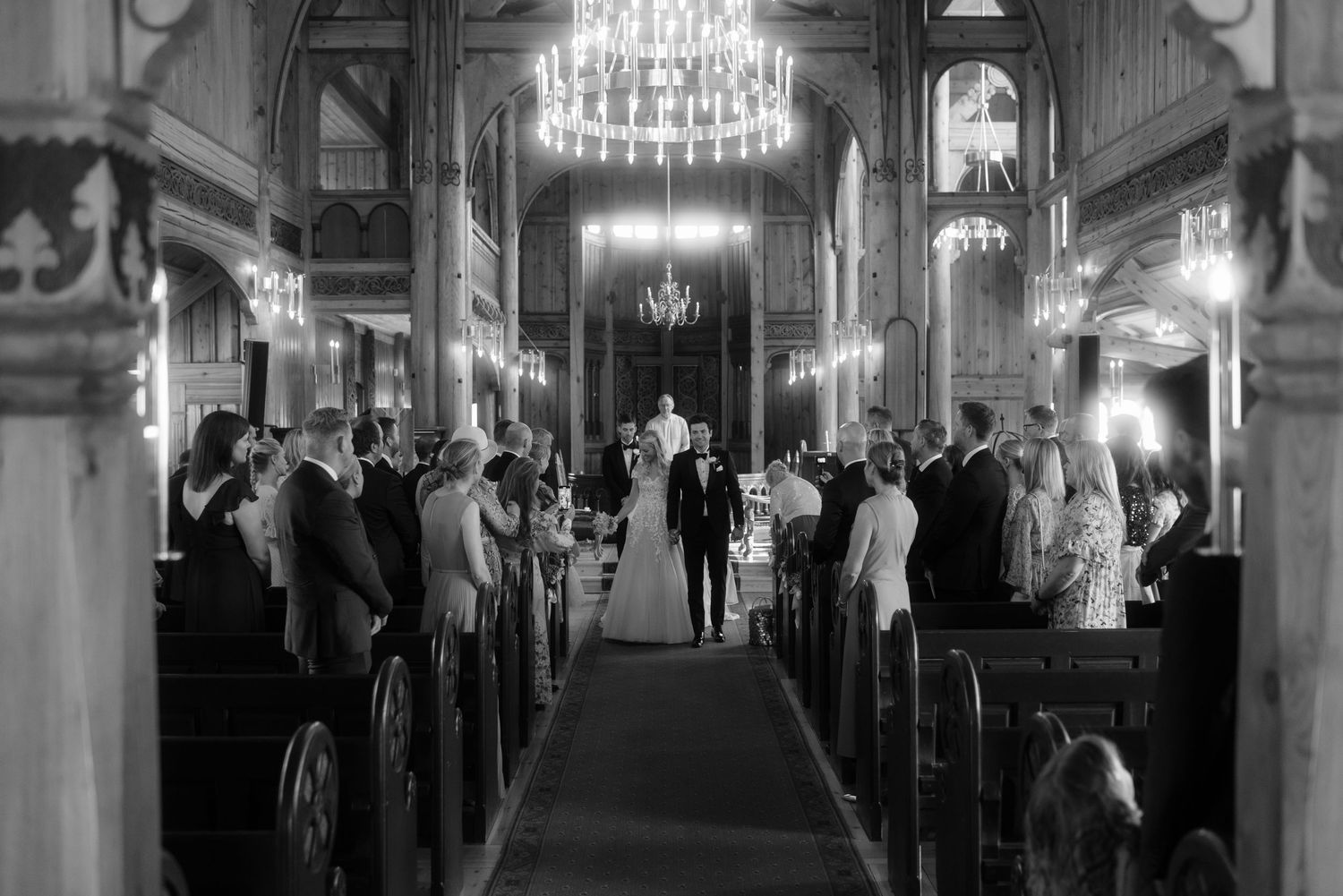 A monochrome image of a church wedding ceremony with guests seated in wooden pews.