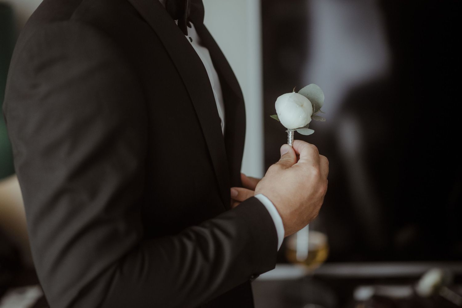 Person in a dark suit adjusting a white boutonniere flower.