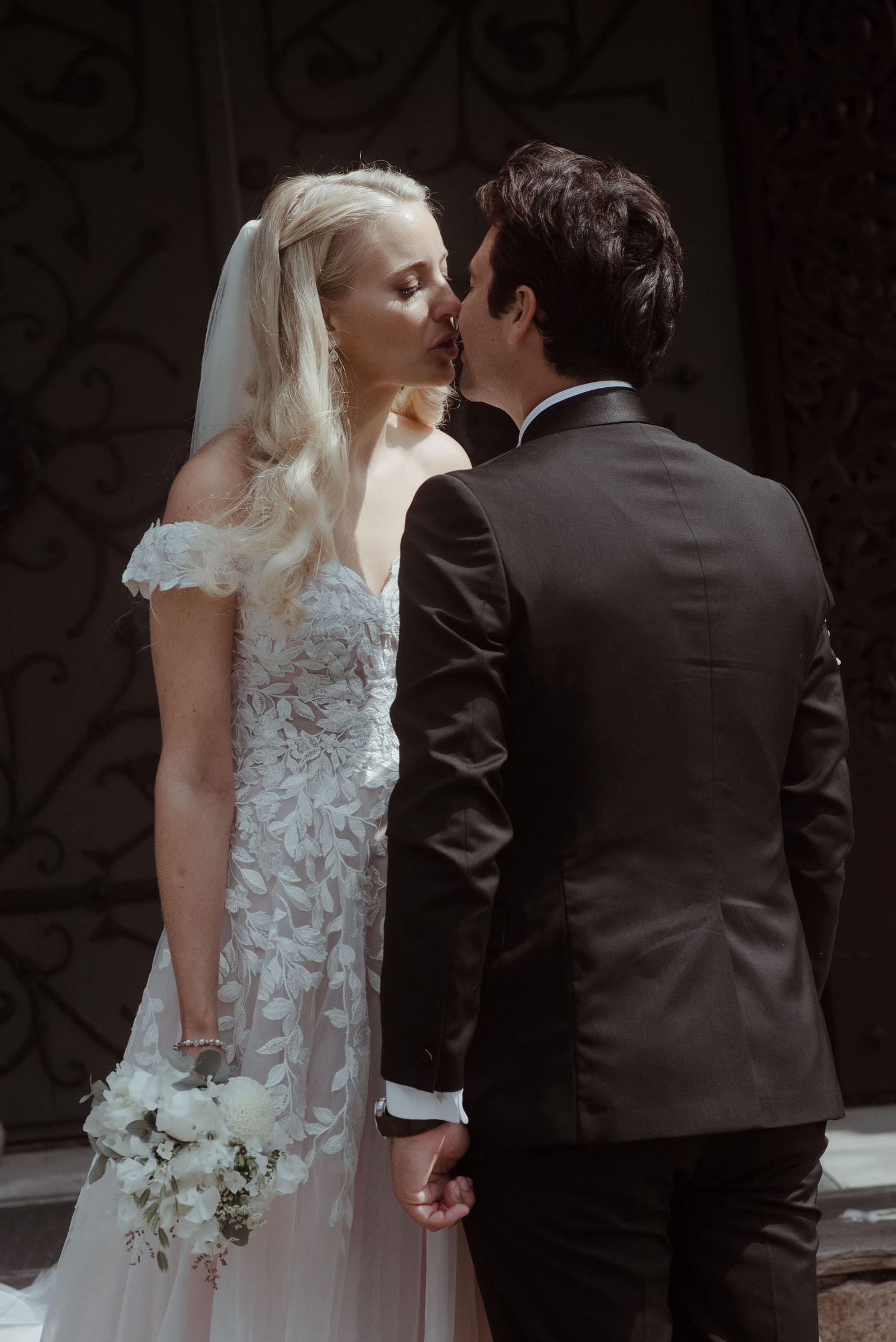 An intimate wedding kiss captured against an ornate dark background.