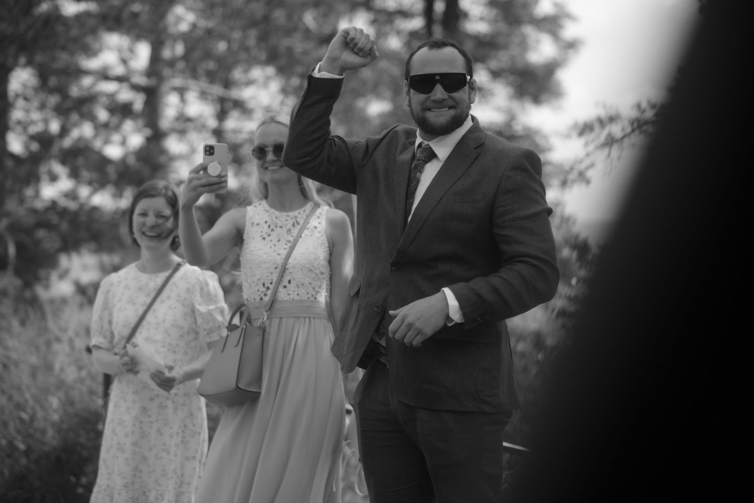 Wedding guests in formal attire celebrating outdoors in a black and white photo.