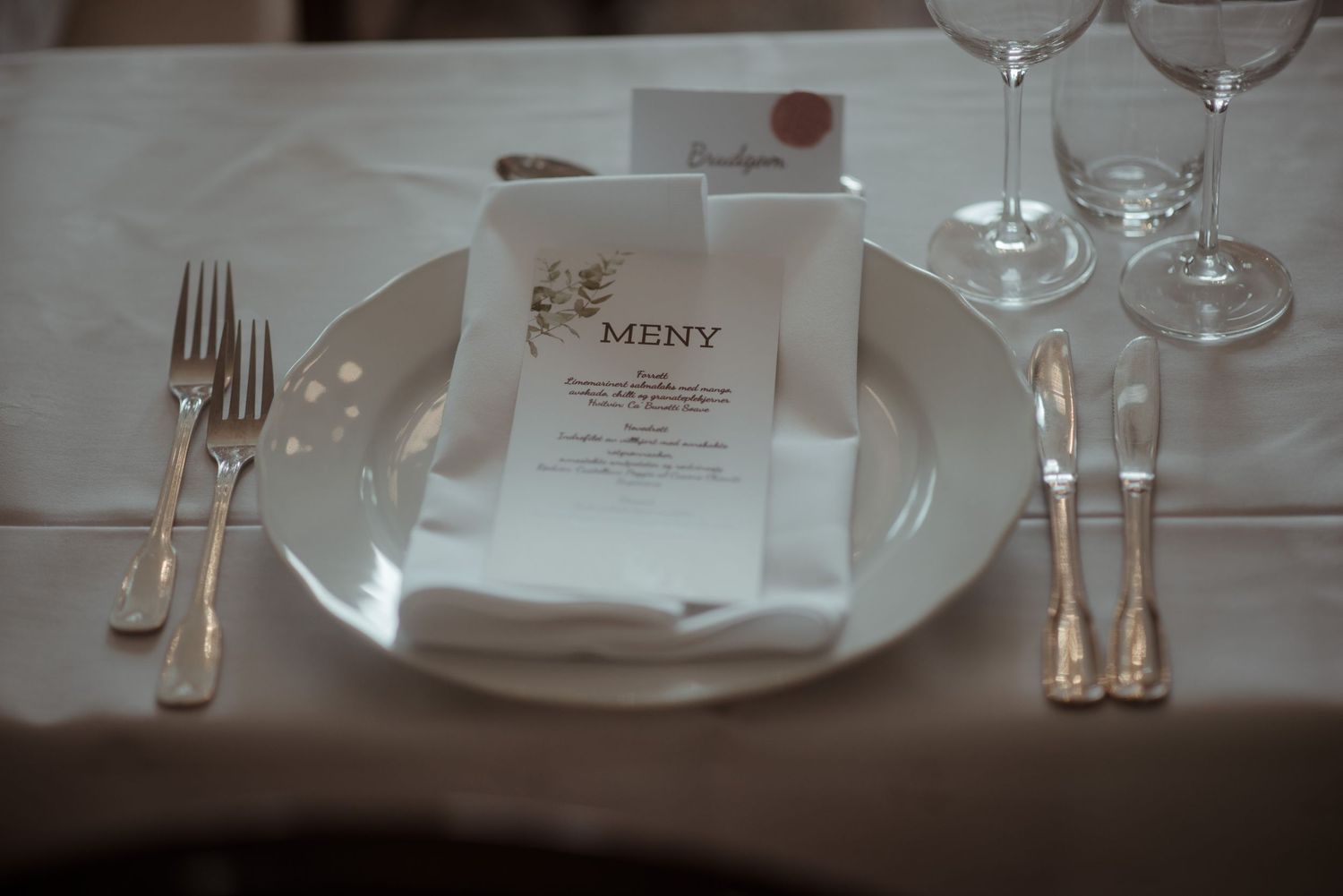 Formal place setting with menu card and silverware on white tablecloth.