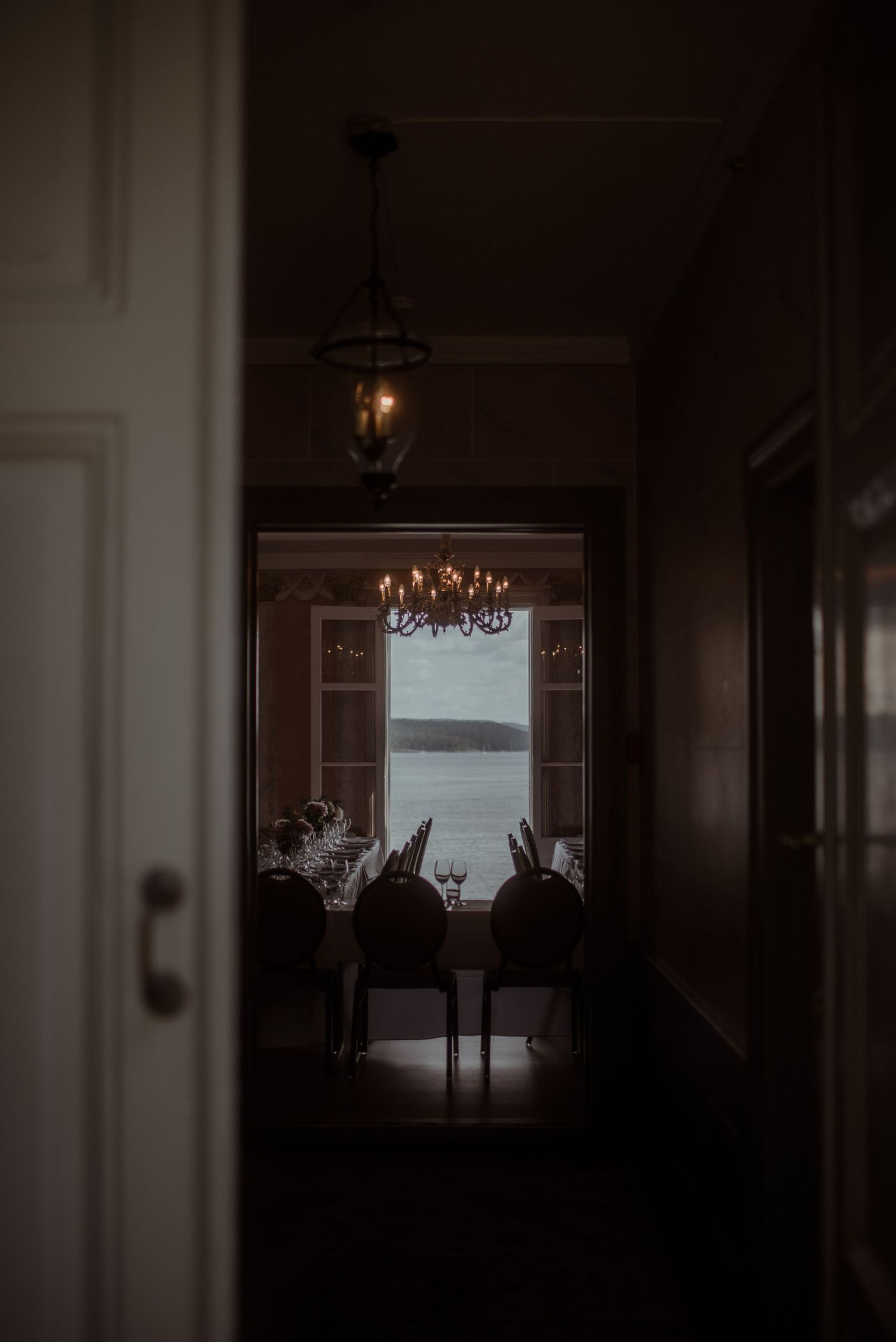 Dark moody interior hallway with chandelier and window showing water view.