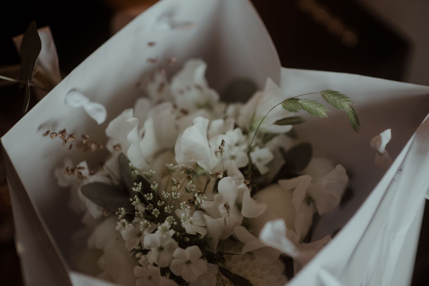 Delicate white floral bouquet with mixed flowers and greenery in soft, moody lighting.
