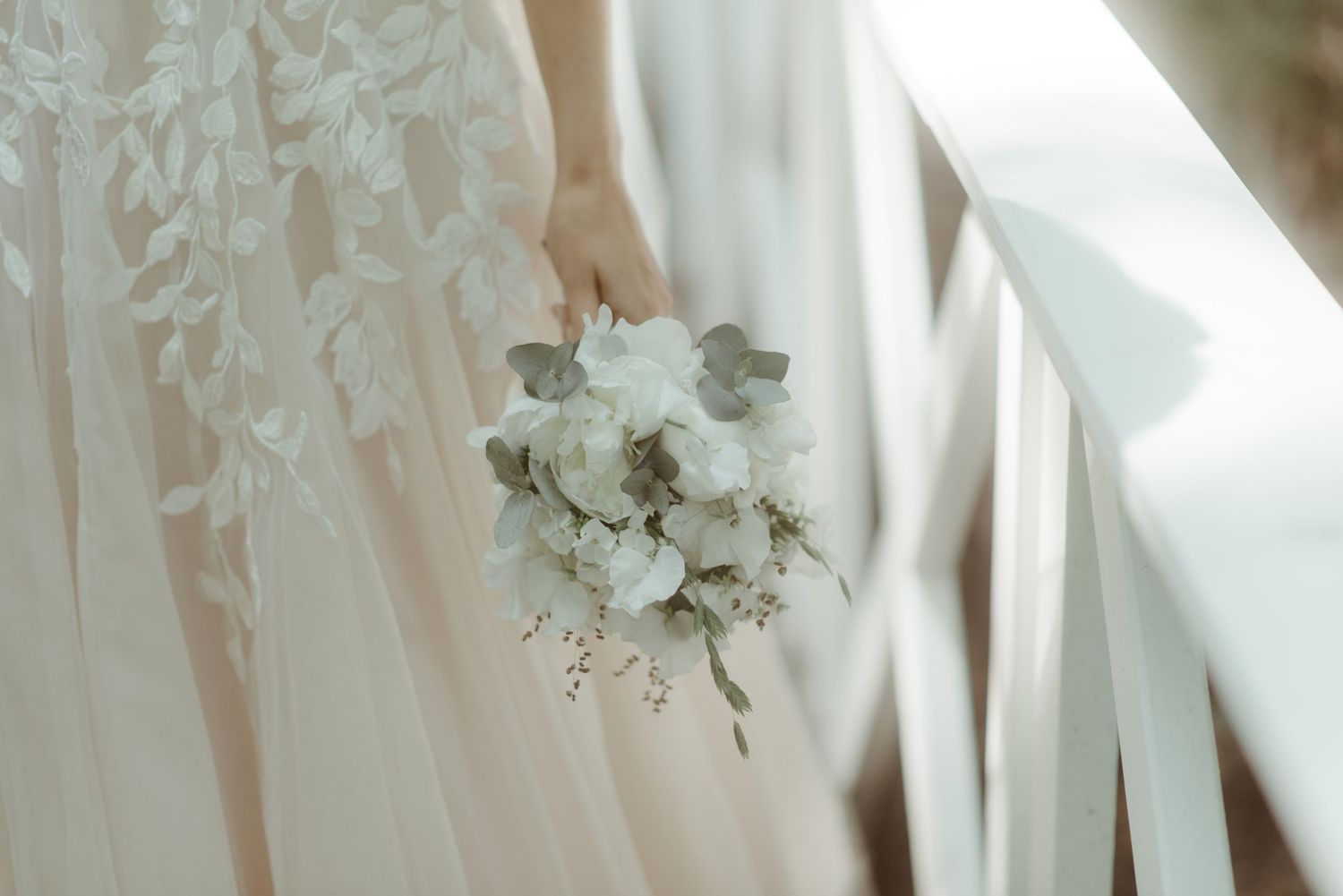 A delicate white and green bridal bouquet held against a flowing wedding dress.