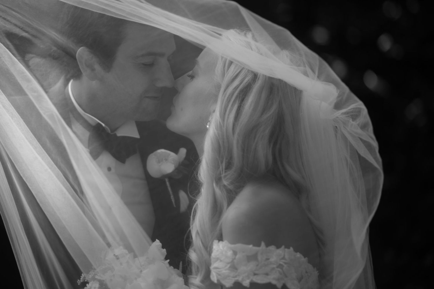 A tender wedding moment captured under a flowing veil in classic black and white.