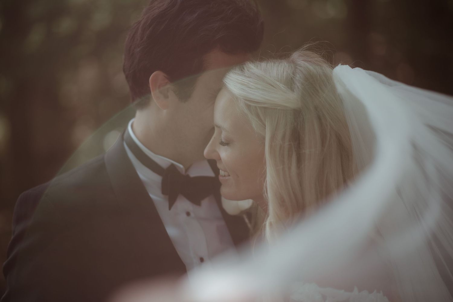 An intimate wedding portrait with soft focus and flowing veil creating a dreamy atmosphere.