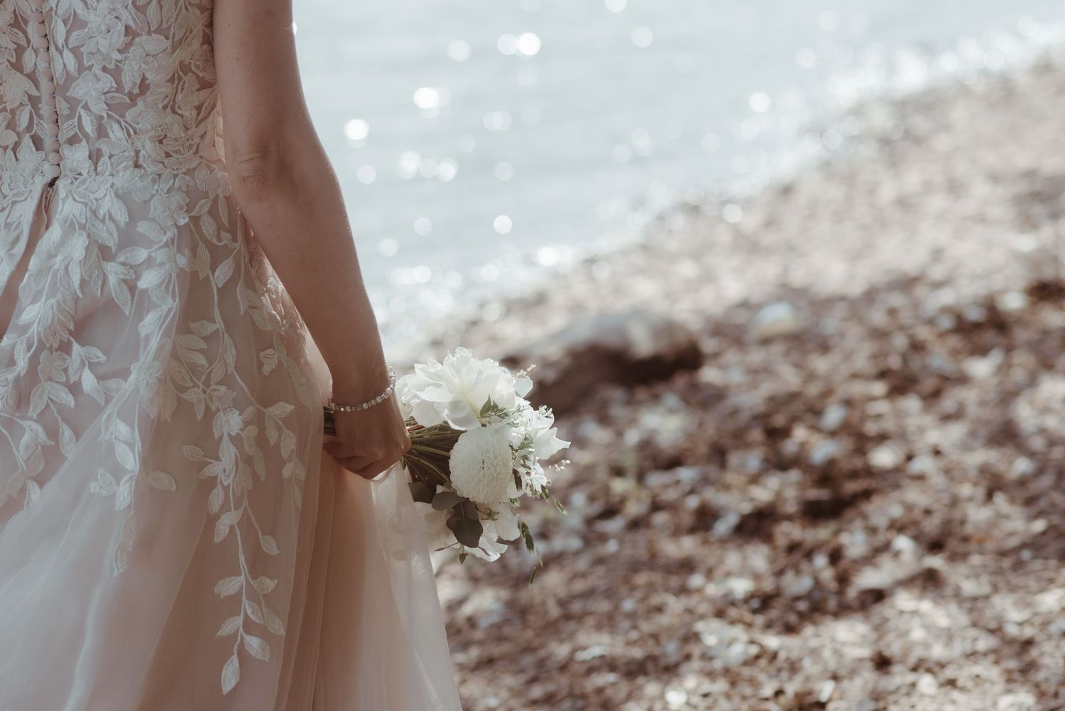 A close-up detail shot of a bride holding a white bouquet against her lace wedding dress.