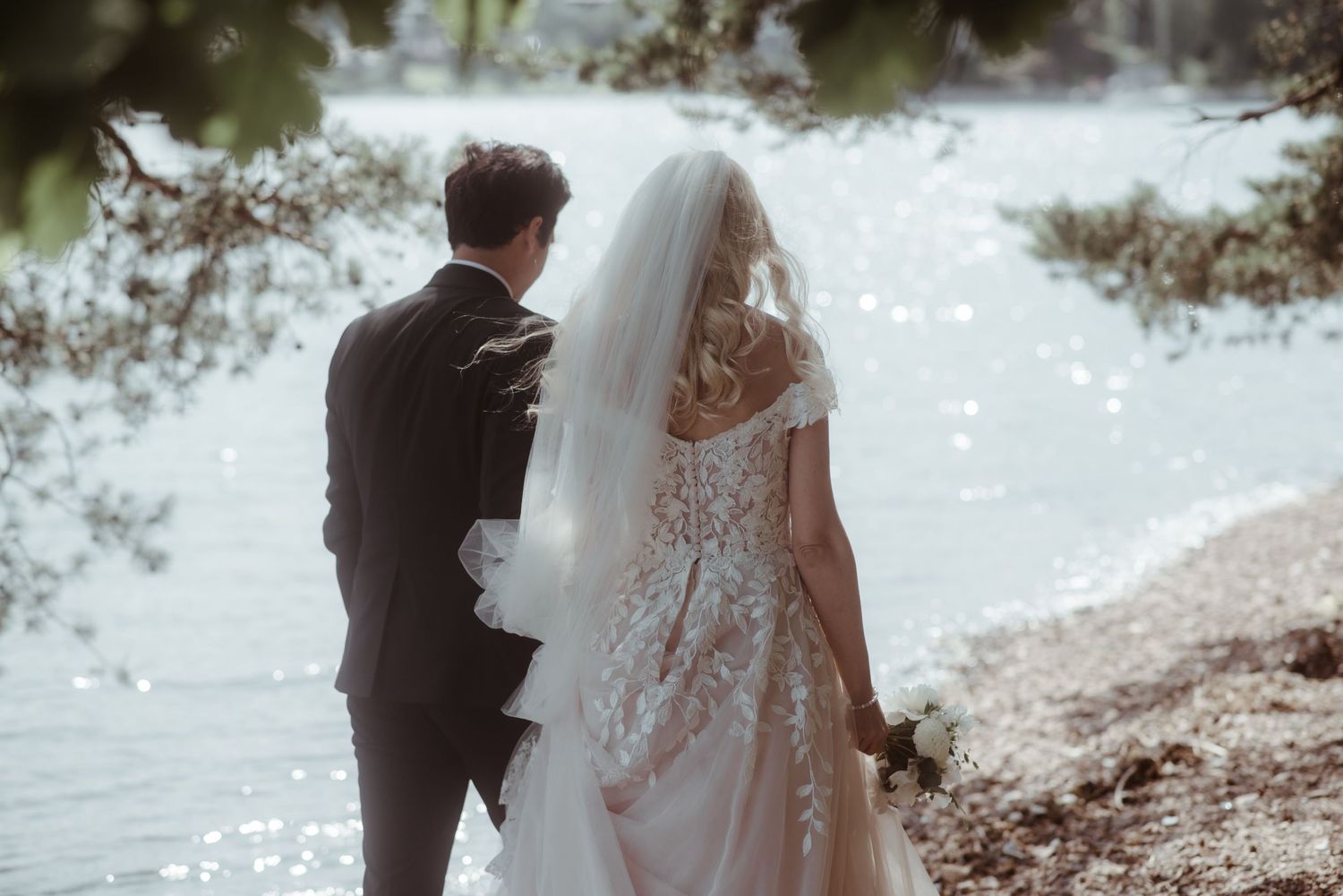 A romantic waterfront wedding portrait showing the couple's formal attire from behind.