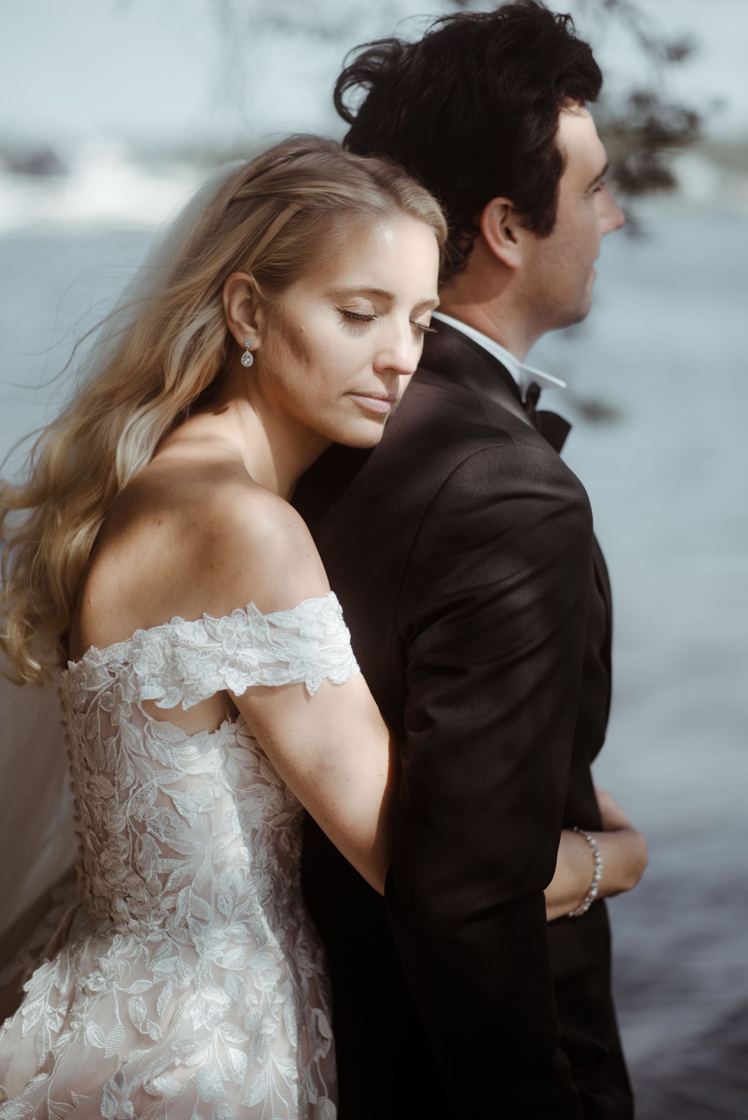 An intimate wedding portrait of a couple in formal attire by the water.