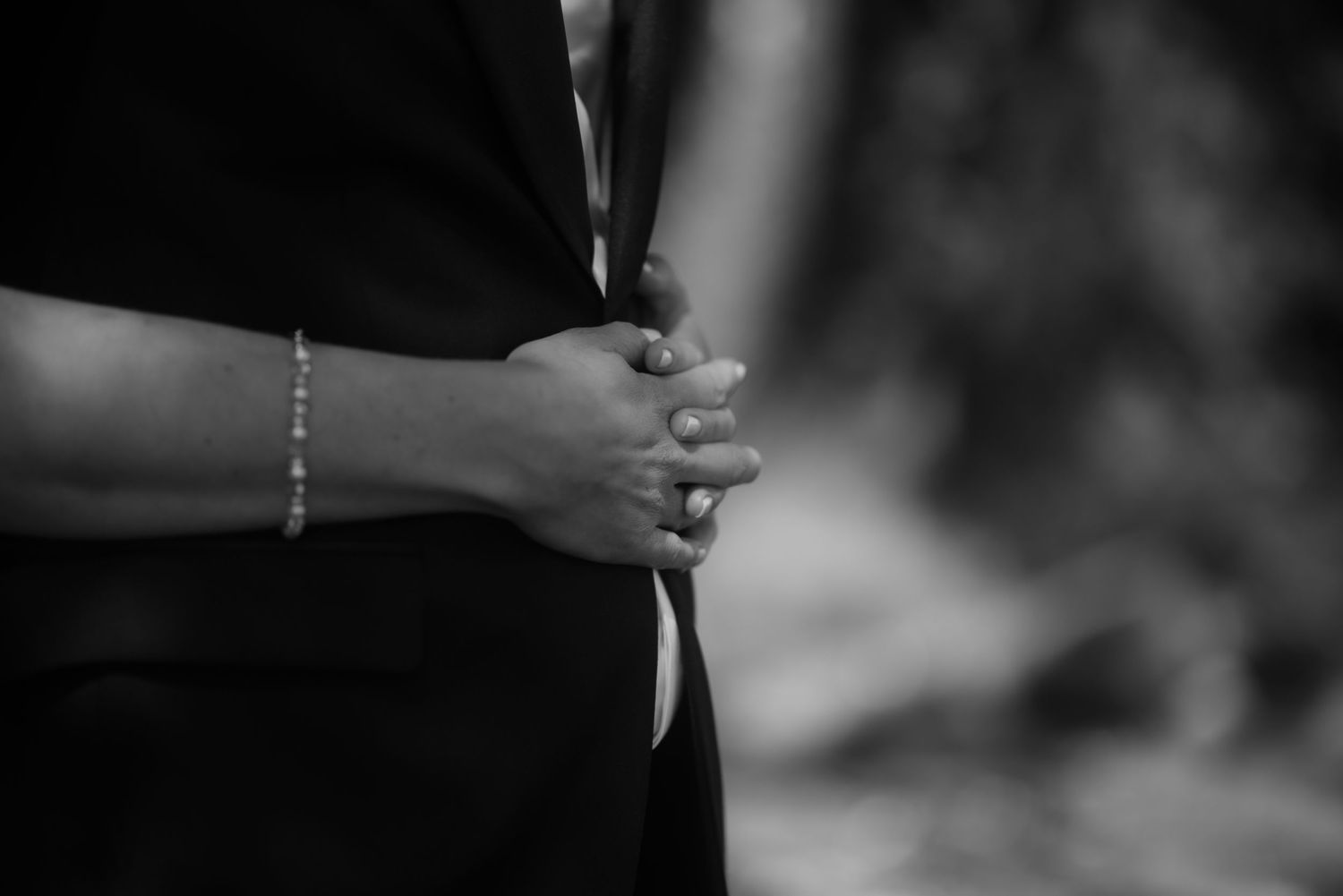 A black and white close-up of clasped hands during a wedding ceremony.