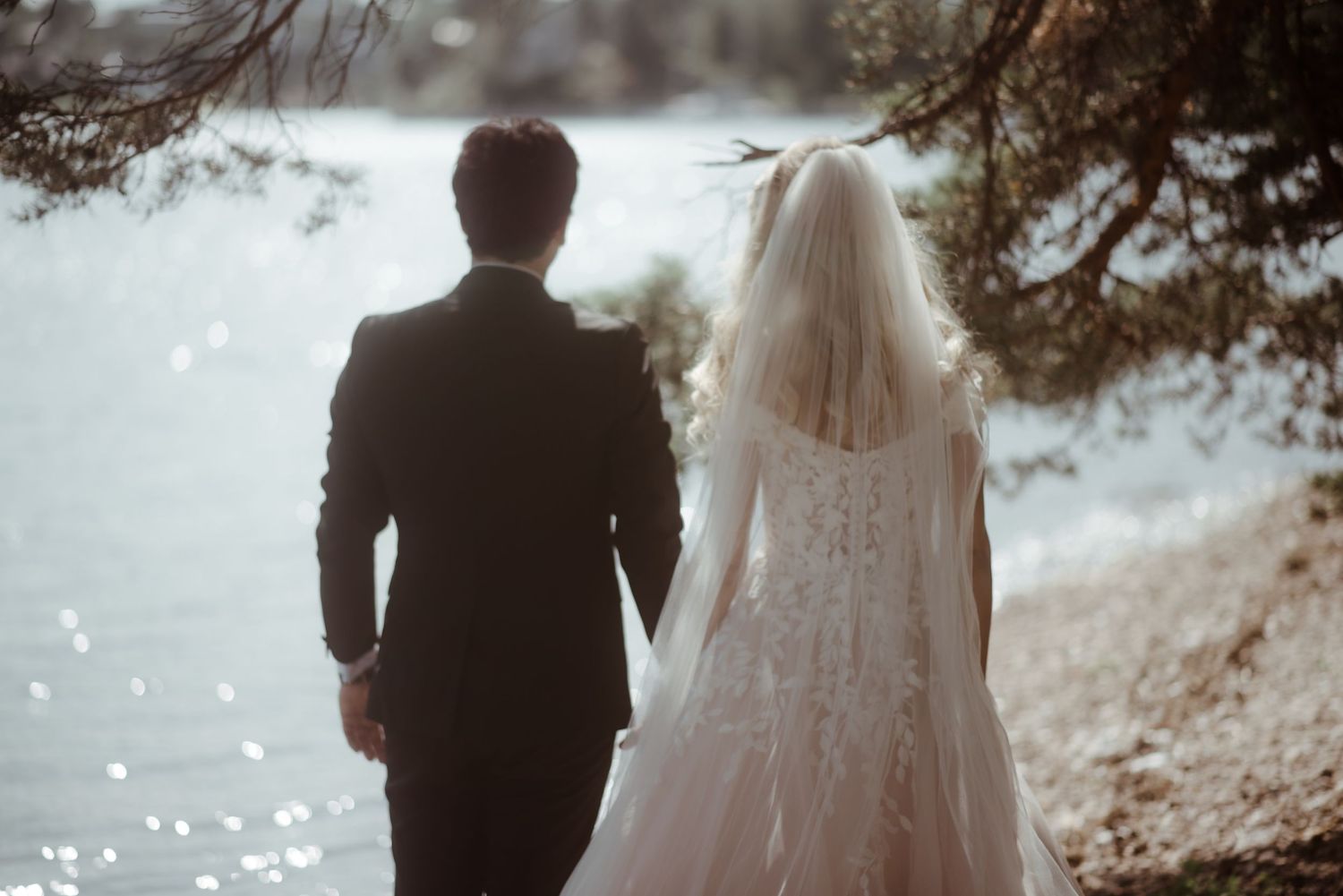 A silhouetted wedding couple stands together overlooking sparkling water.