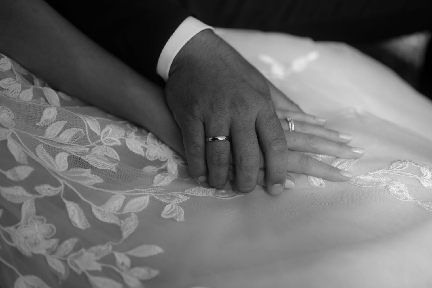 Two hands with wedding rings rest gently on white lace fabric.