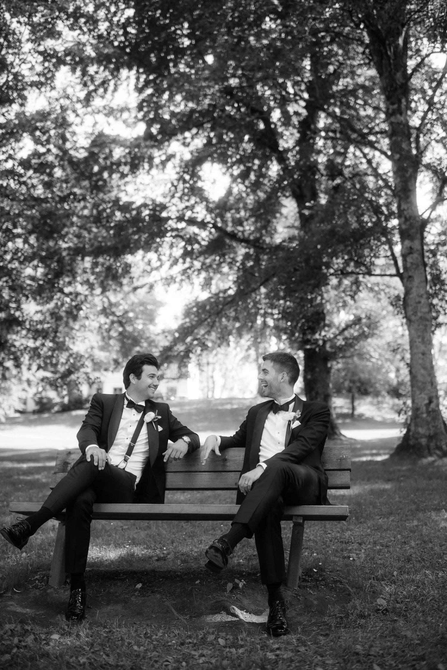 A black and white photo of two people chatting on a bench in a leafy park.