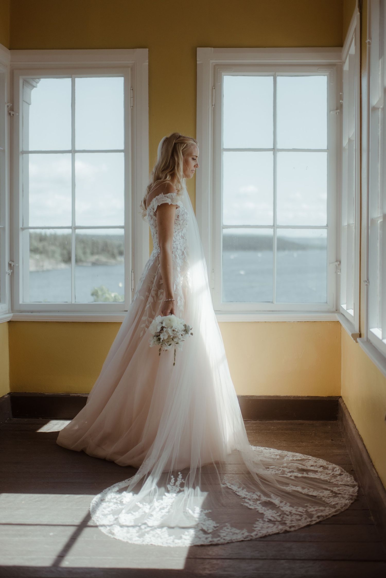 Elegant white wedding gown with long train photographed in front of bright windows.