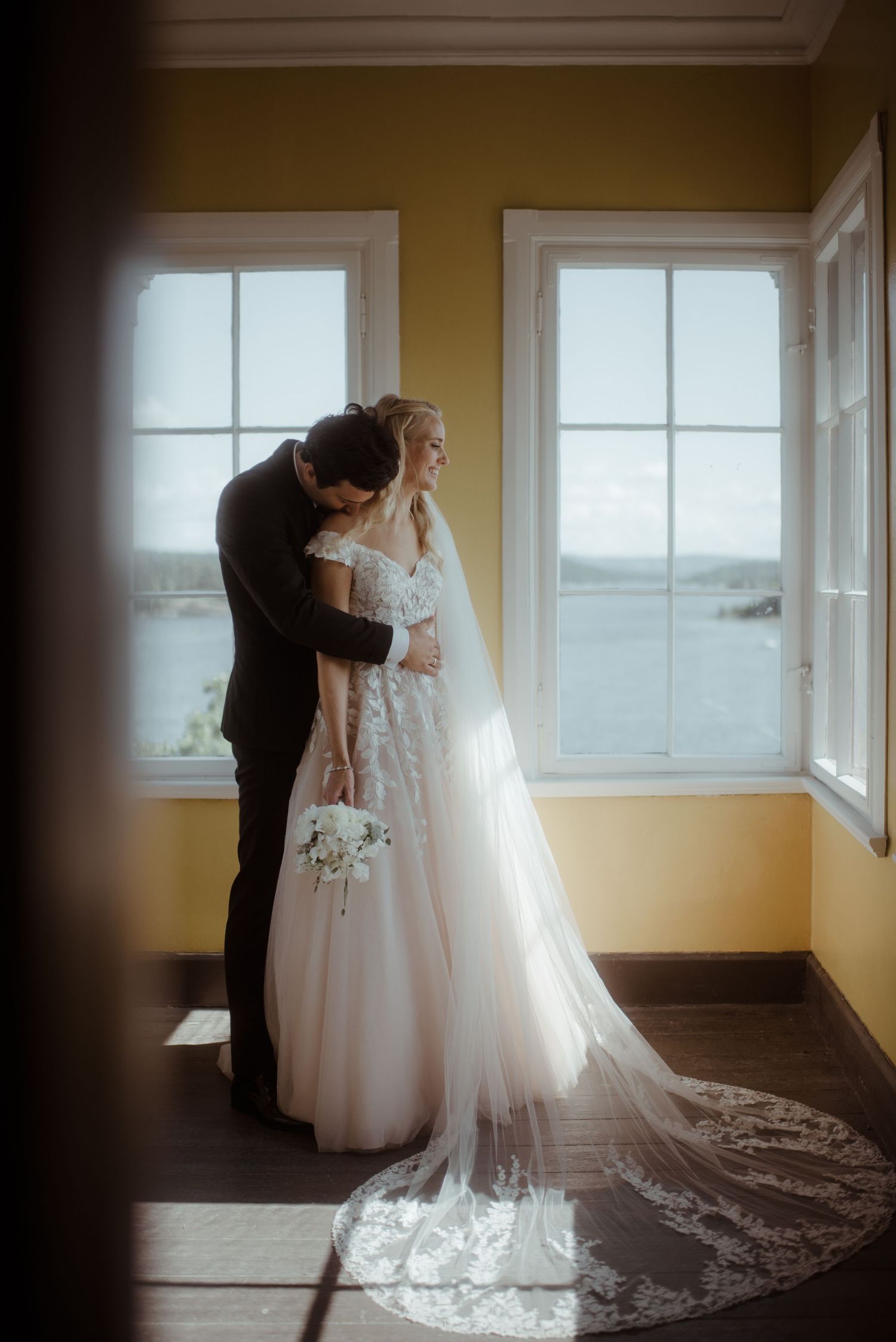 Intimate wedding moment captured in a sun-filled room with yellow walls.