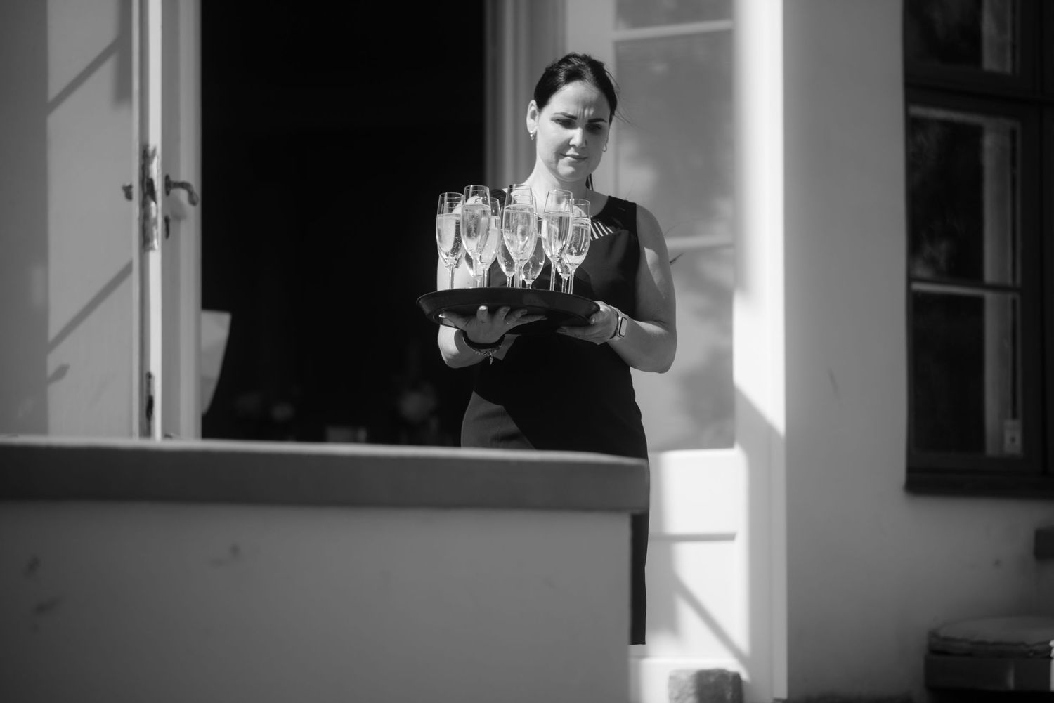 Black and white photo of server carrying tray in dramatic window lighting.
