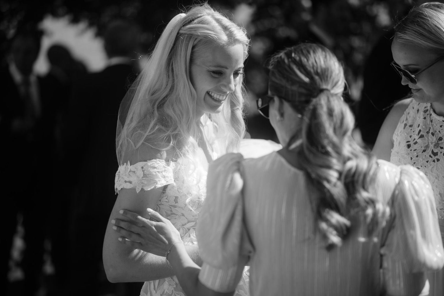 A wedding celebration outdoors with guests in summer attire and bright natural lighting.