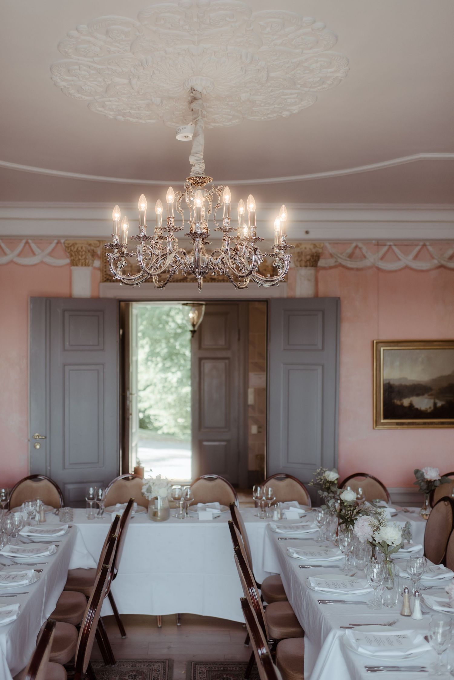An elegant dining room with crystal chandelier and white-clothed tables set for a formal event.