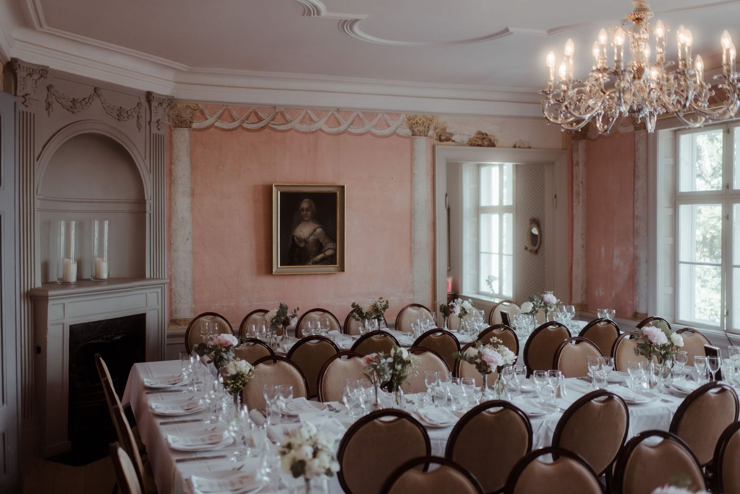 A formal dining room with peach walls, ornate chandelier and round tables set for a wedding reception.