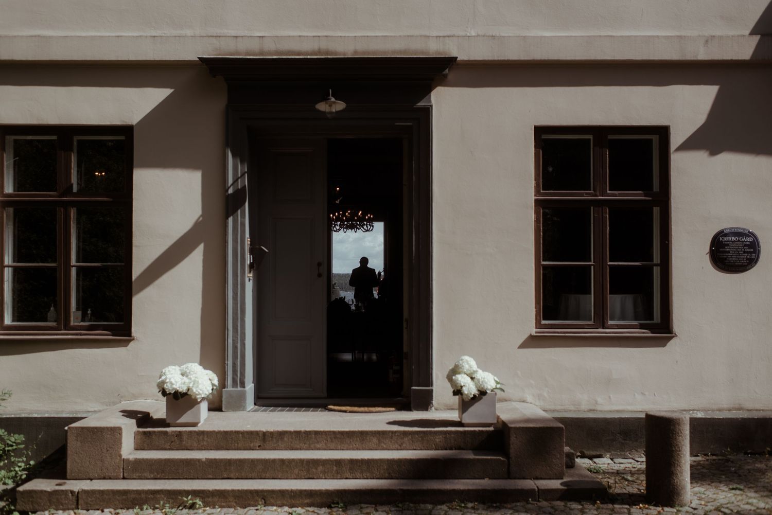 White building entrance with symmetrical windows and flower decorations on the front steps.