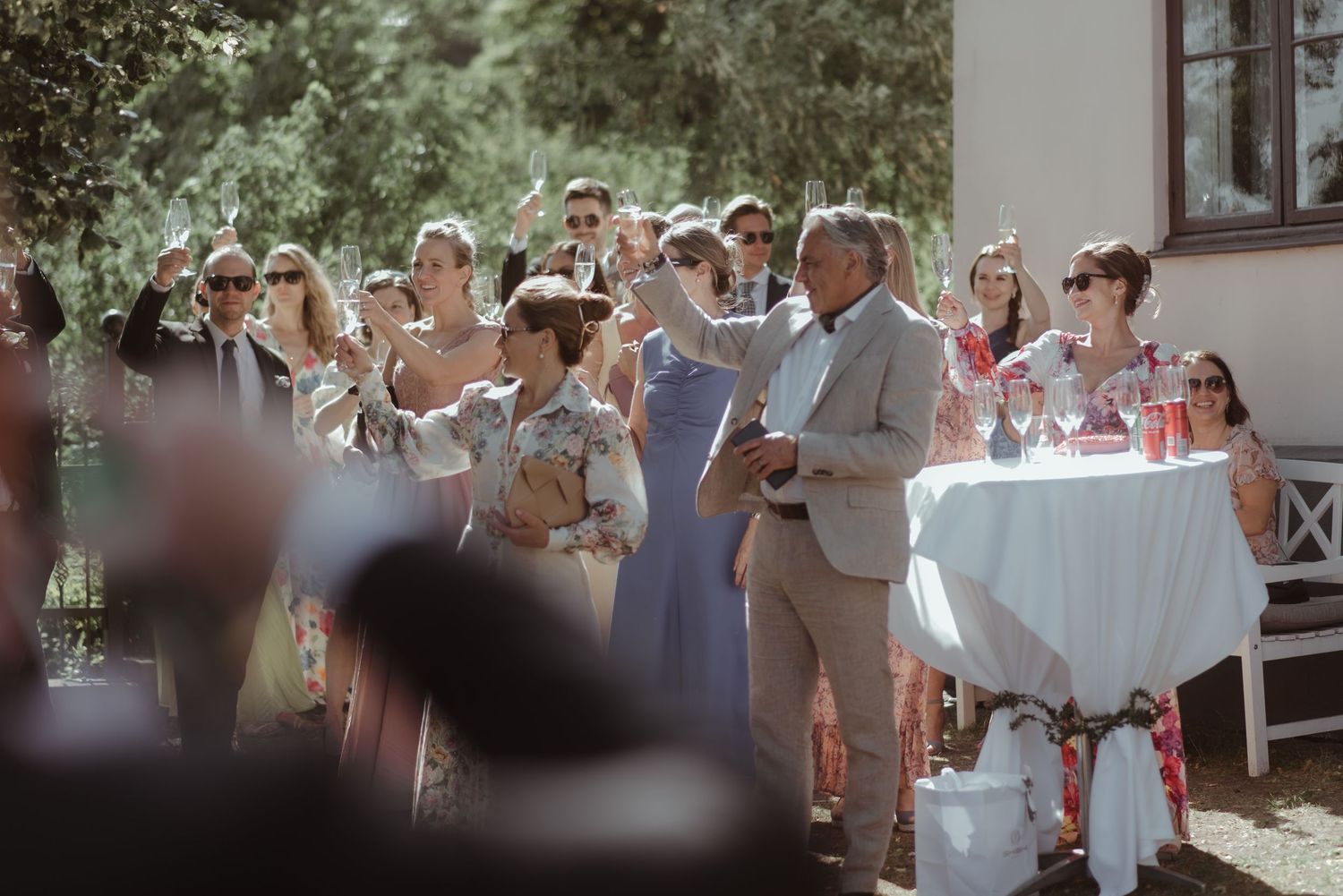Outdoor wedding reception with guests mingling around decorated tables in natural sunlight.