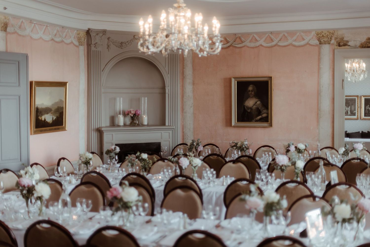 Elegant ballroom with crystal chandelier, antique paintings, and formal dining tables set for a grand occasion.