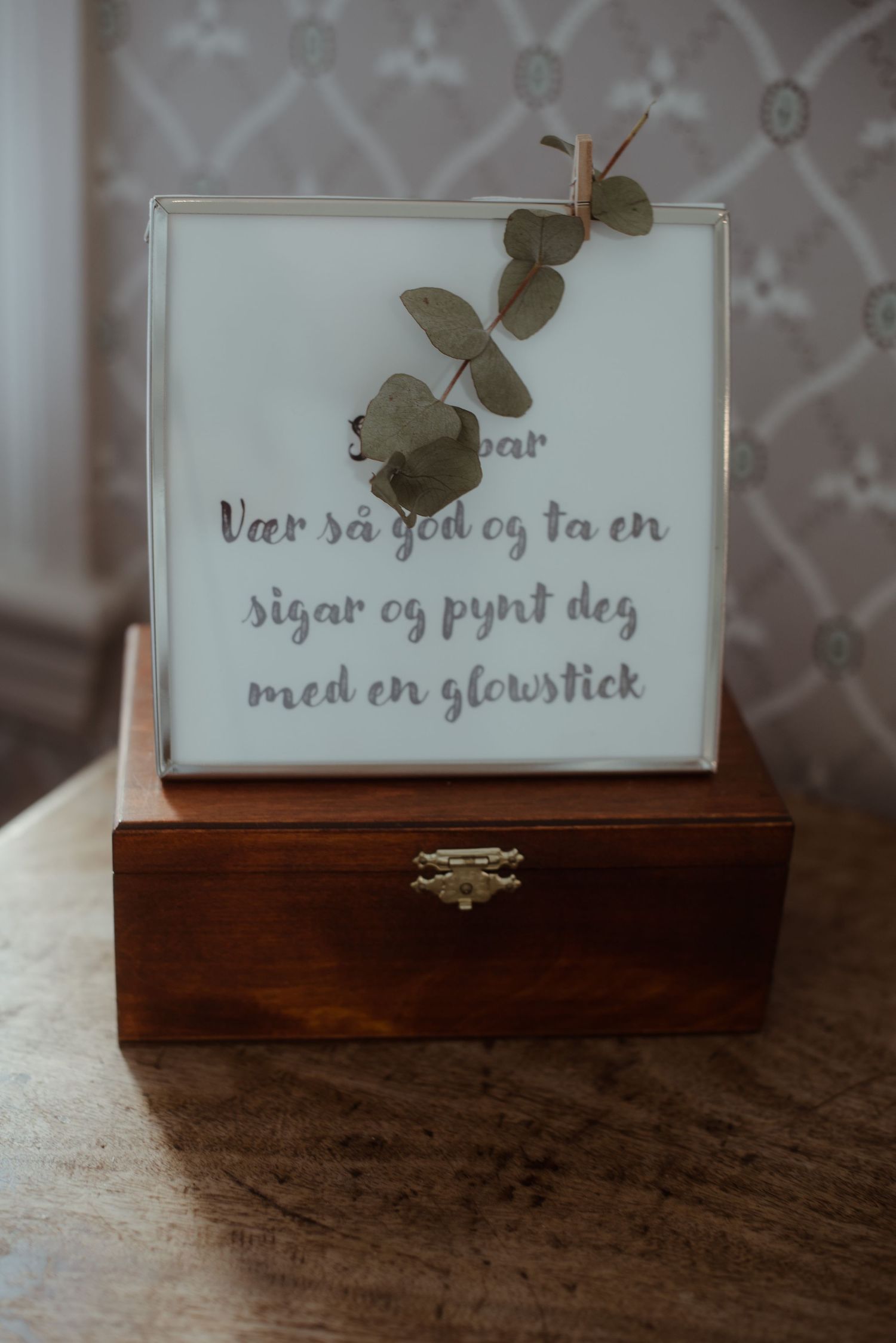 Wooden box with decorative text and eucalyptus sprig on white surface.