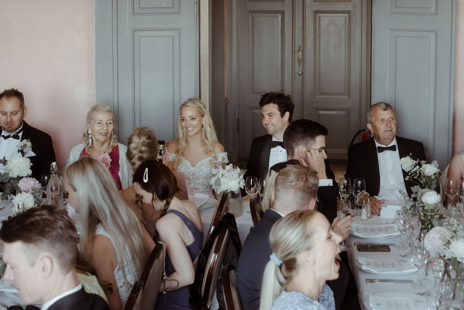 Formal dining setup with floral centerpieces and guests seated at elegant tables.