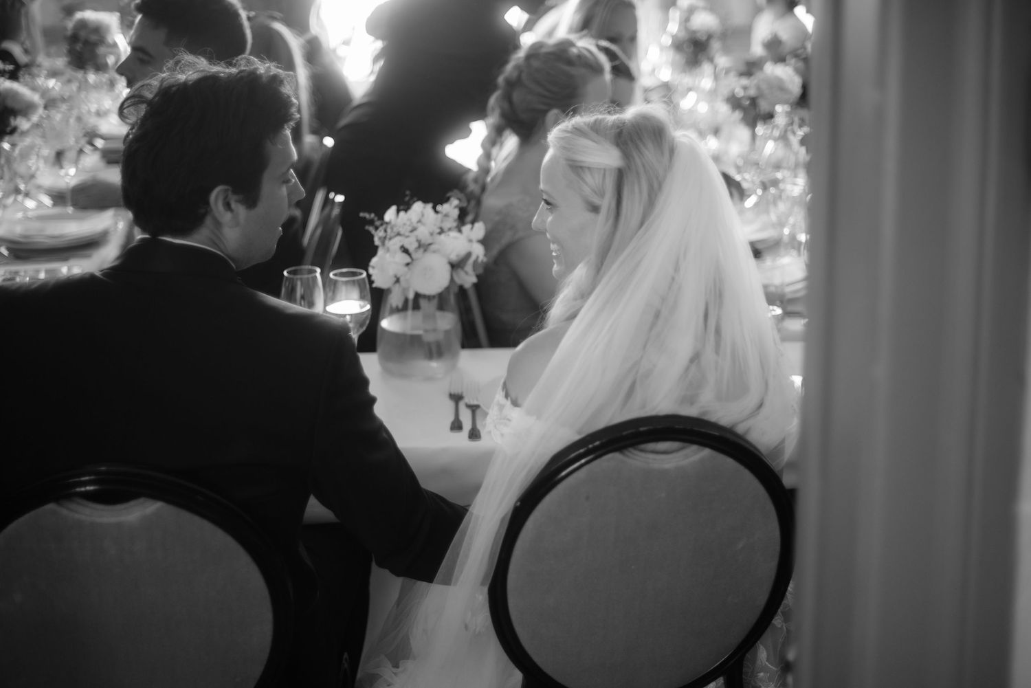 Black and white photograph of an intimate wedding reception moment at a dining table.