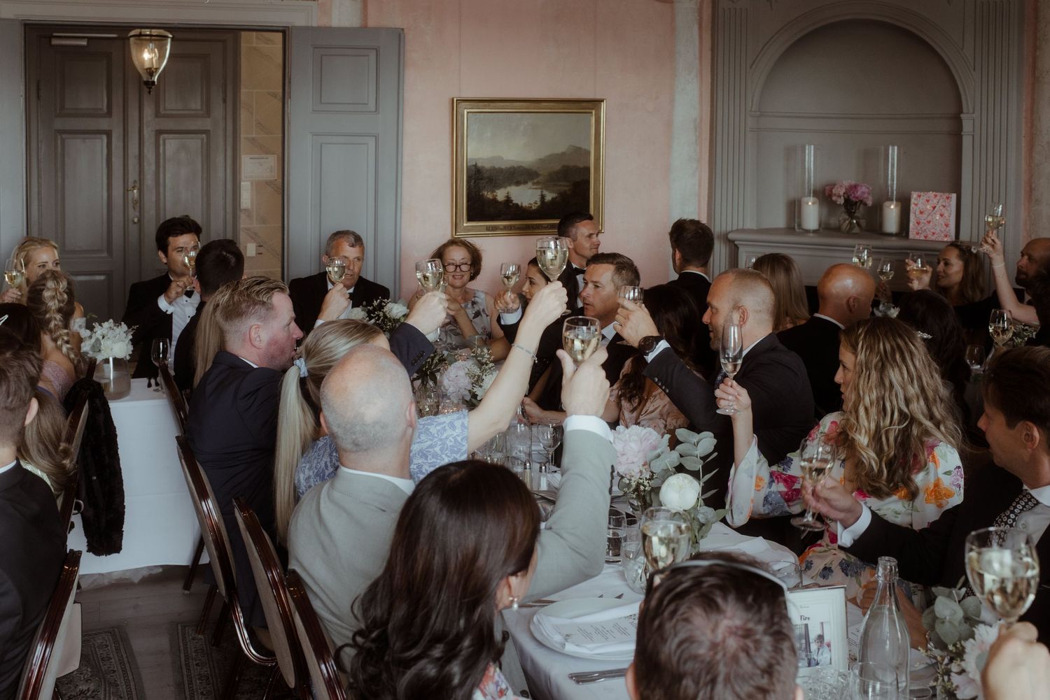 Reception guests raising glasses in celebration inside an elegant room with classic decor.
