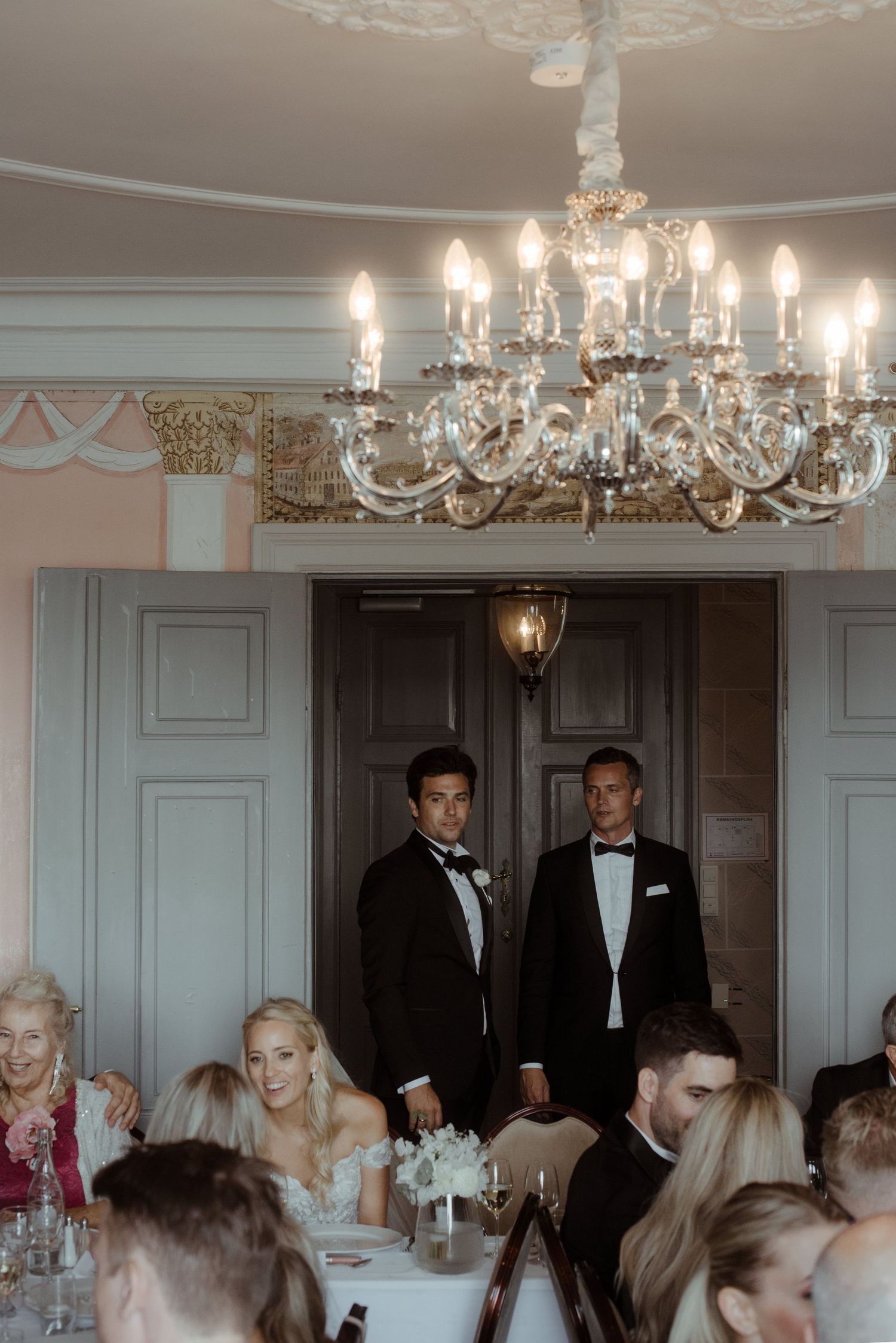 An ornate crystal chandelier illuminates a formal dining room during an elegant event.