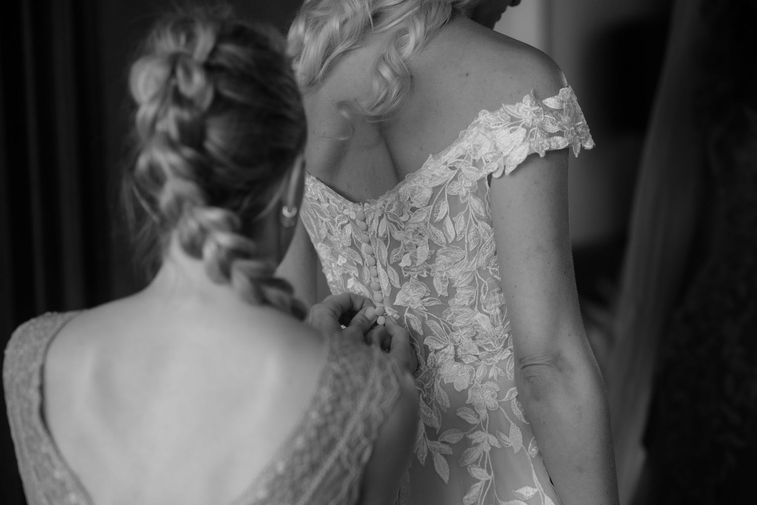 Black and white image showing detailed lace on wedding dress being adjusted.