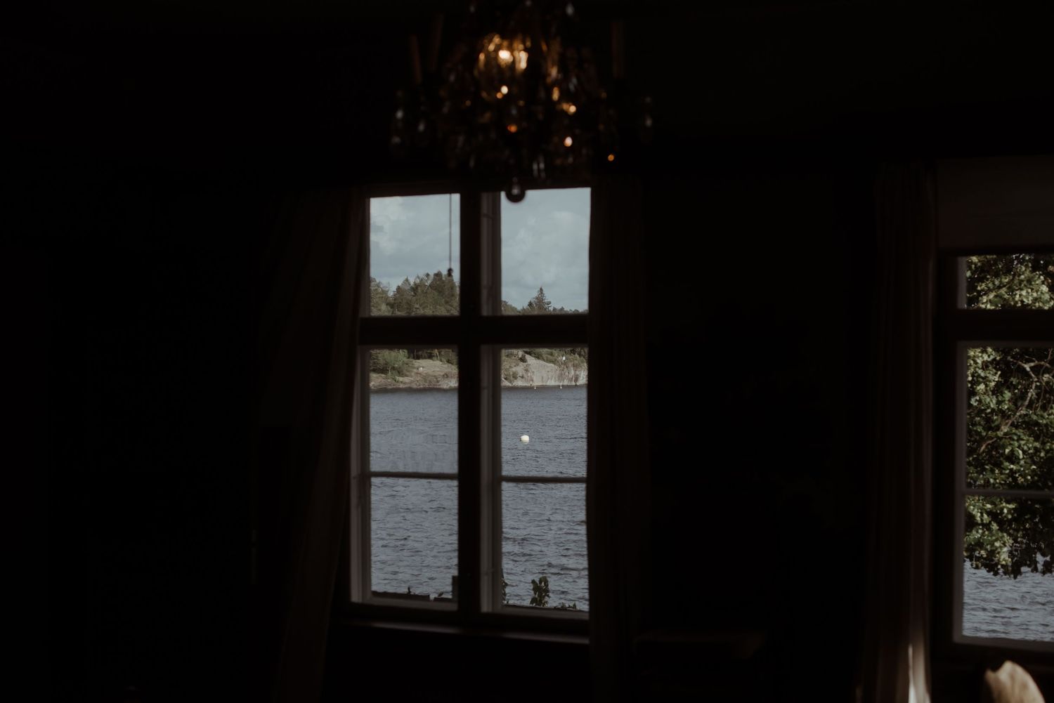 A dark window frame silhouetted against a lake view with pendant lighting.