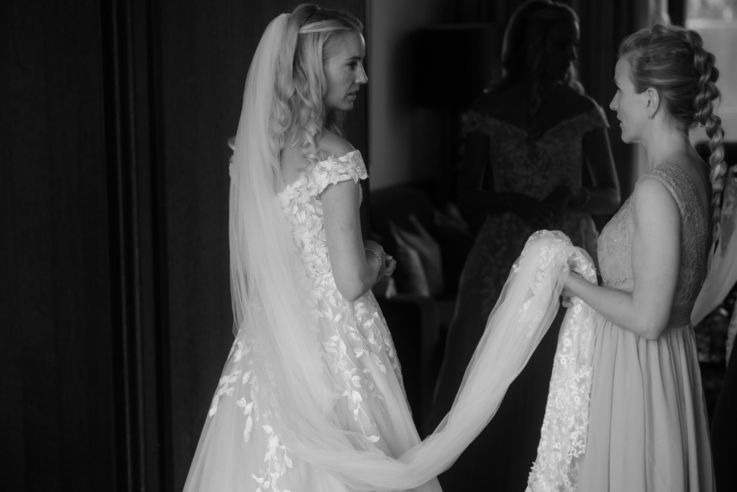 Black and white photo of wedding dress being fitted with help from bridesmaid.