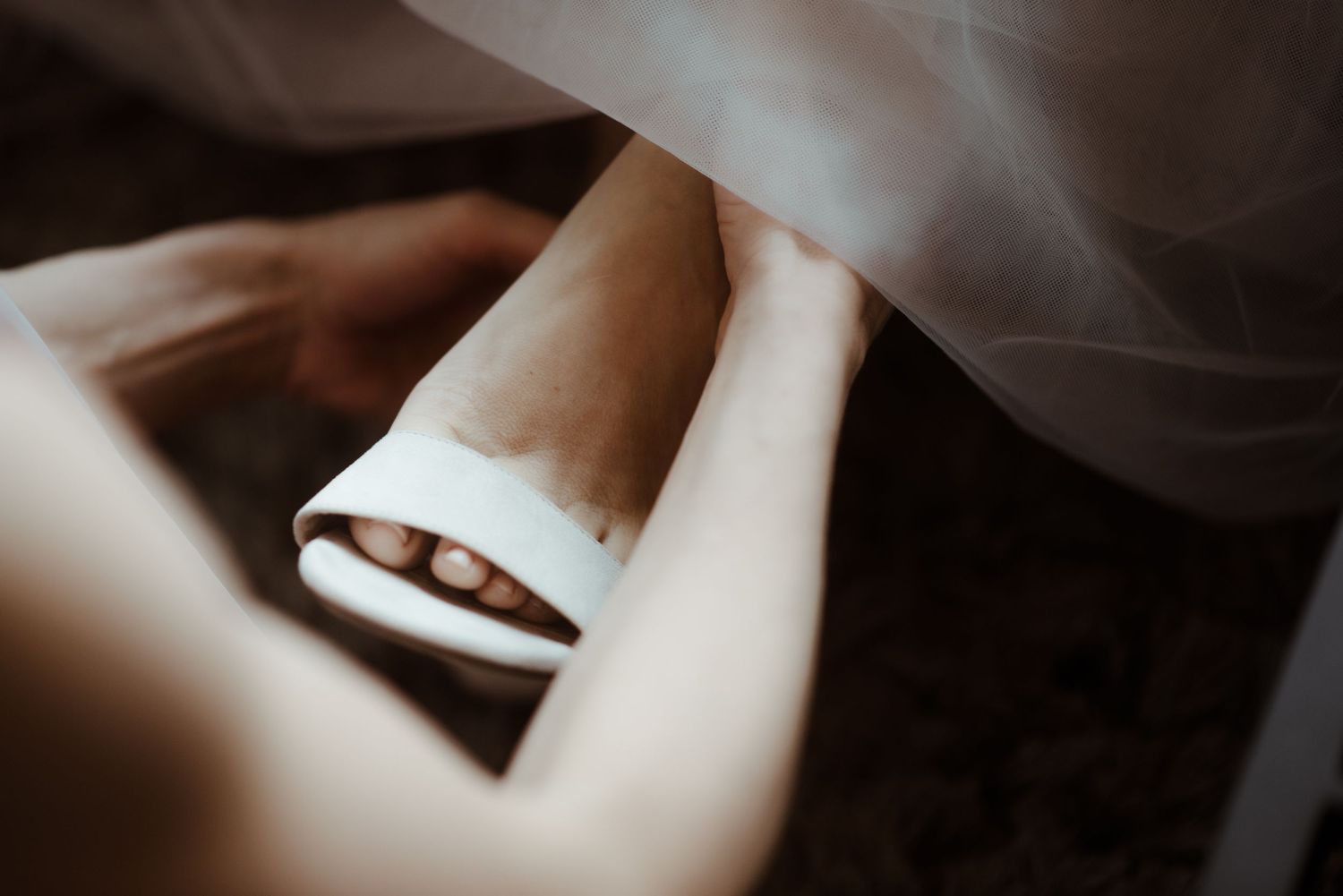 Close-up of white bridal shoe being put on under flowing dress fabric.