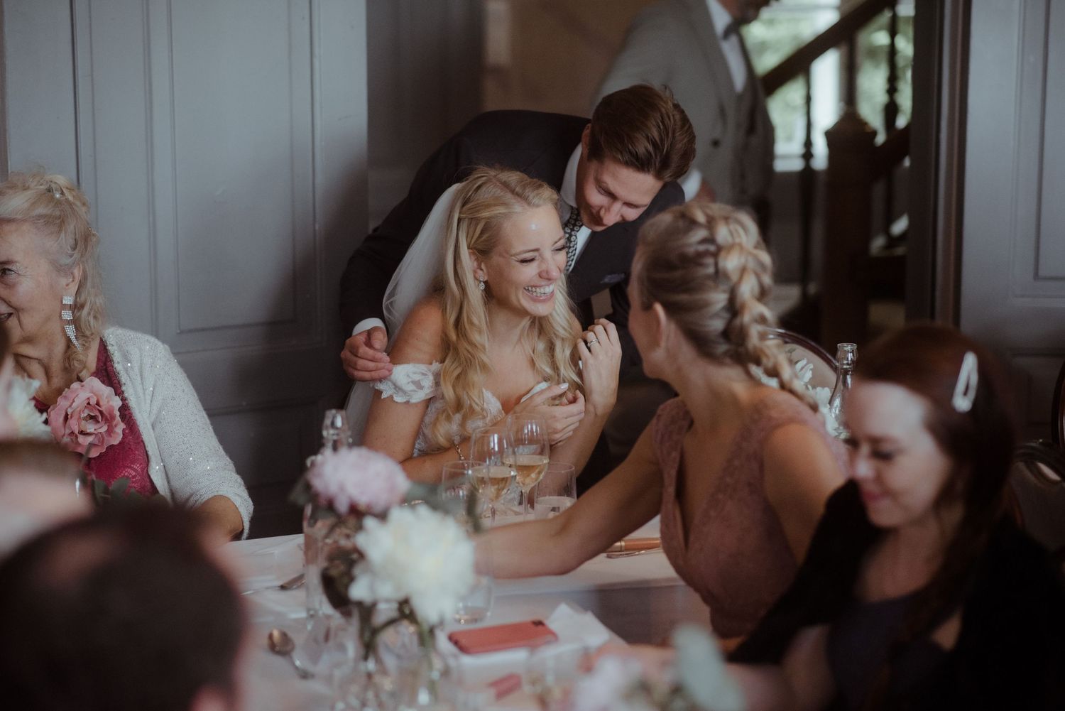 Wedding reception scene with guests gathered around decorated tables indoors.