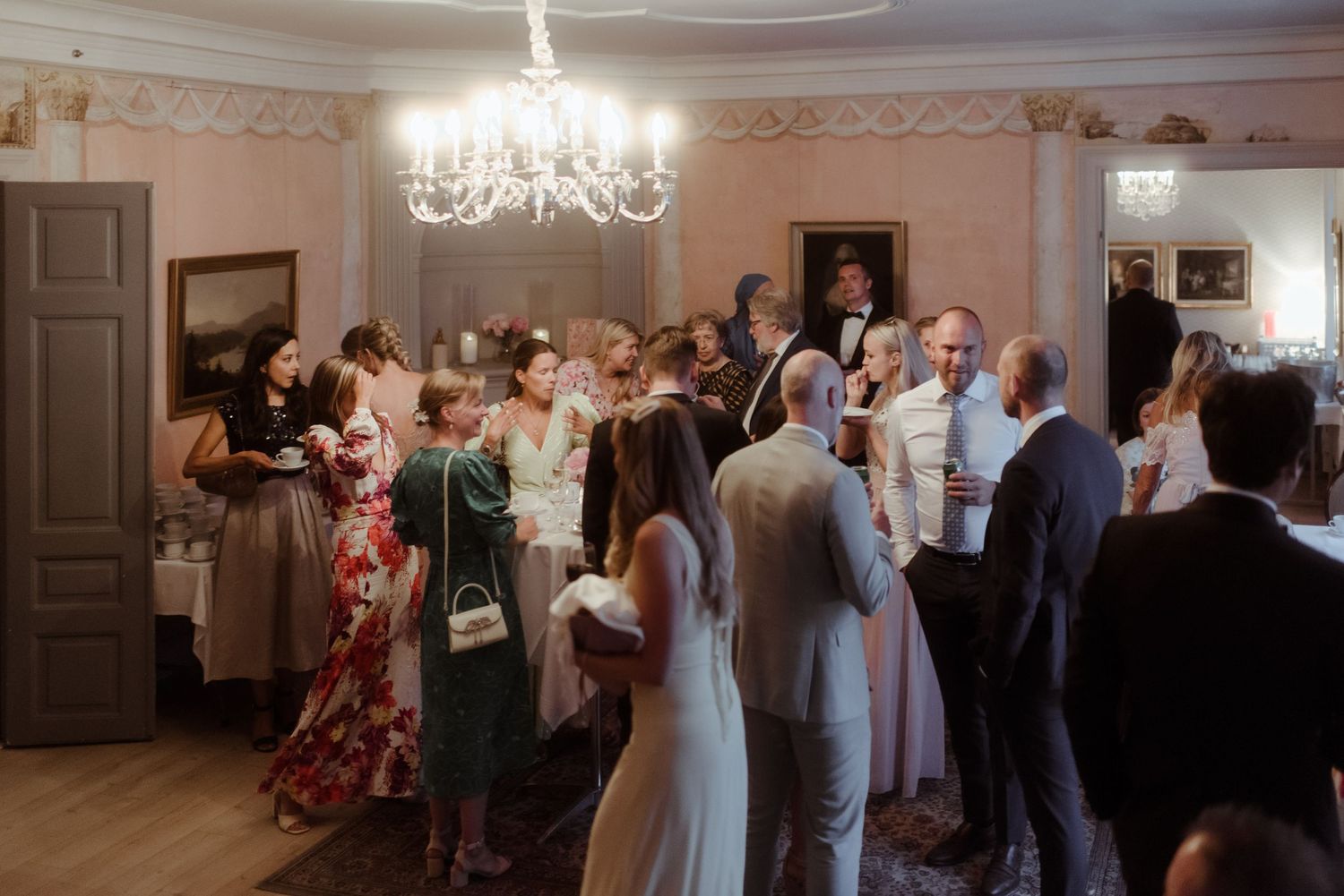 Wedding guests mingle and socialize during an elegant indoor reception with a crystal chandelier.