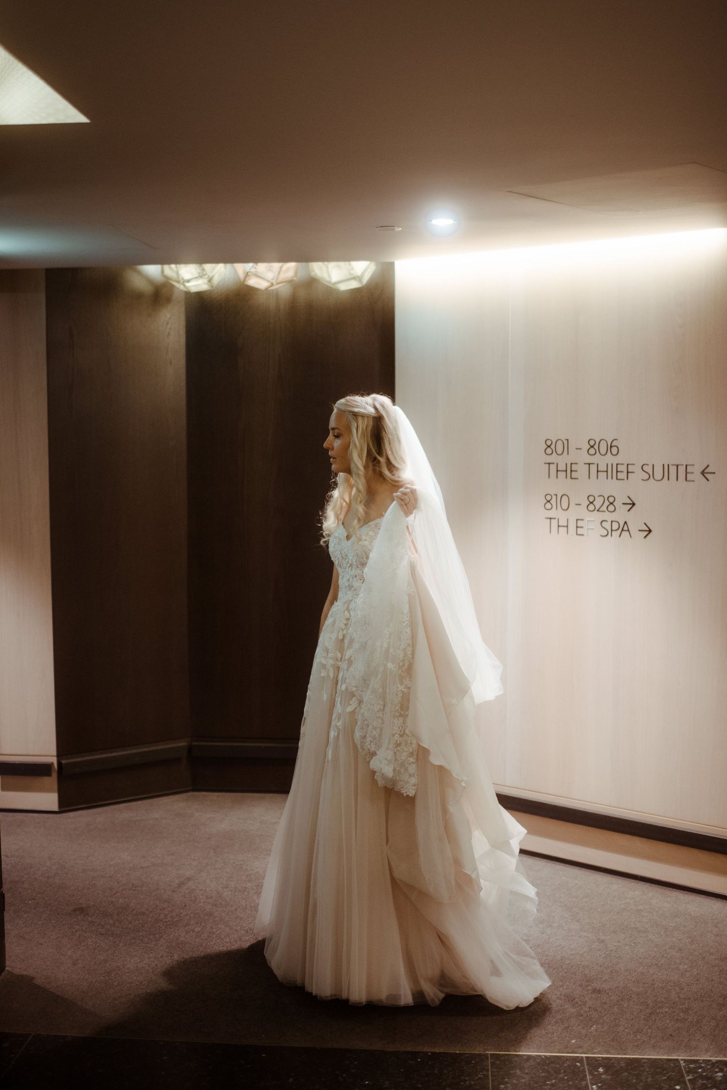 A wedding dress displayed in a hotel hallway showcasing intricate lace details and flowing tulle.